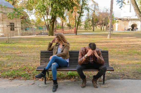 Man and woman sitting on a park bench arguing